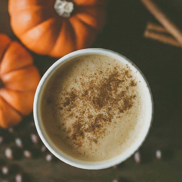 Cozy cup of Pumpkin Spice Flavored Coffee with cinnamon and pumpkins, embodying the warm essence of fall in every sip.