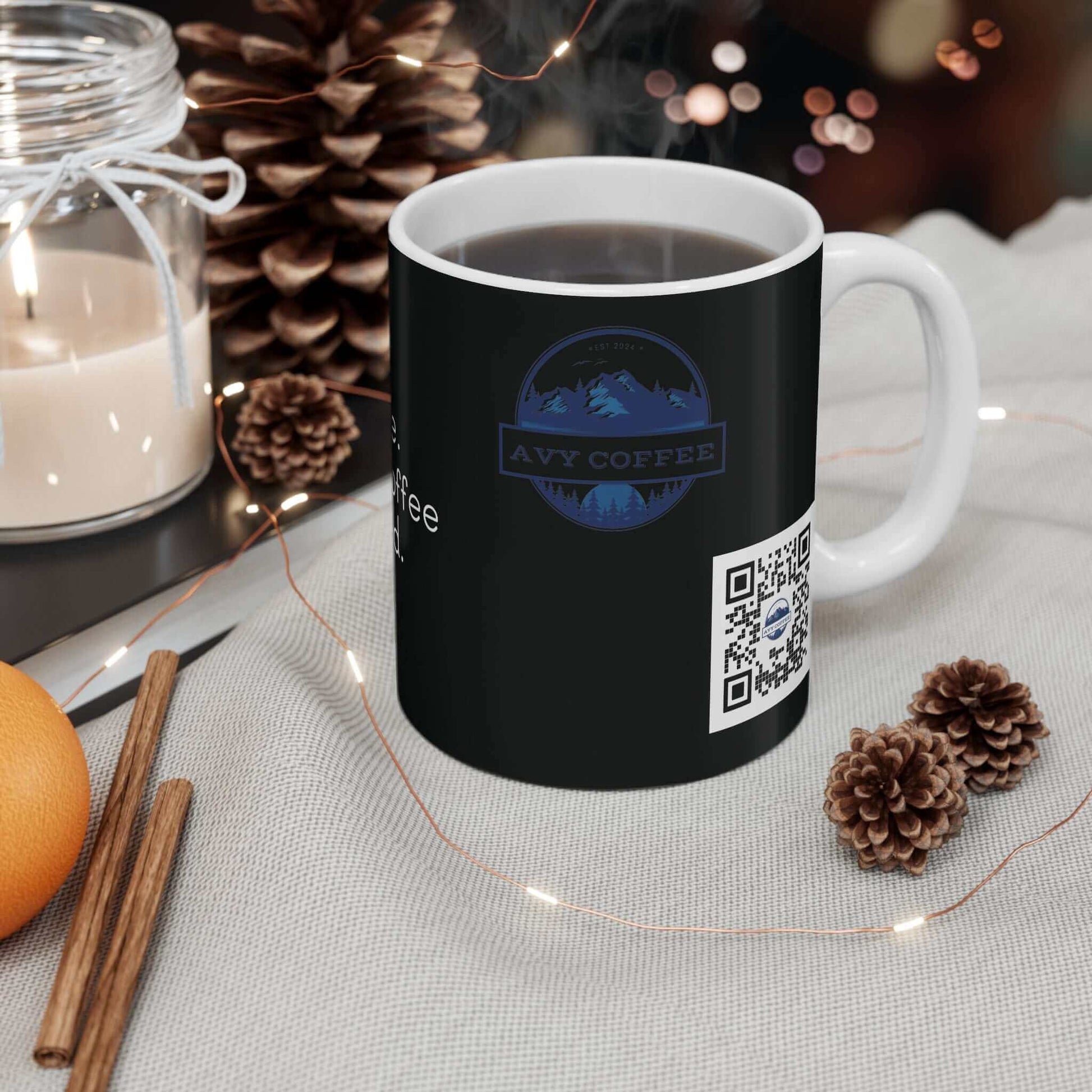 Black coffee mug with "Wait a damn minute" design, 11oz size, white interior, placed on a cozy table setting with pinecones and candles.