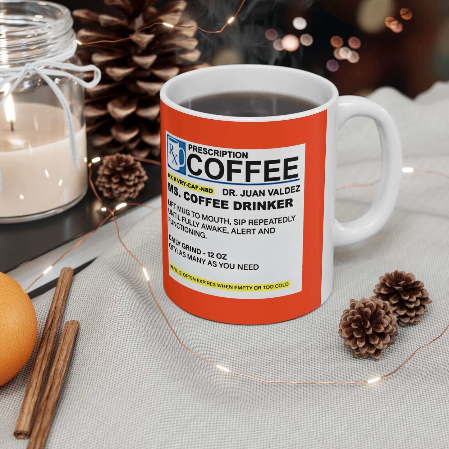 Prescription Coffee Mug - For Her (11oz, 15oz) displayed on a festive table with pinecones, an orange, and lit string lights in the background.