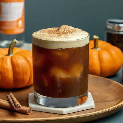 Glass of iced pumpkin spice flavored coffee with cinnamon, surrounded by small pumpkins on a wooden tray.