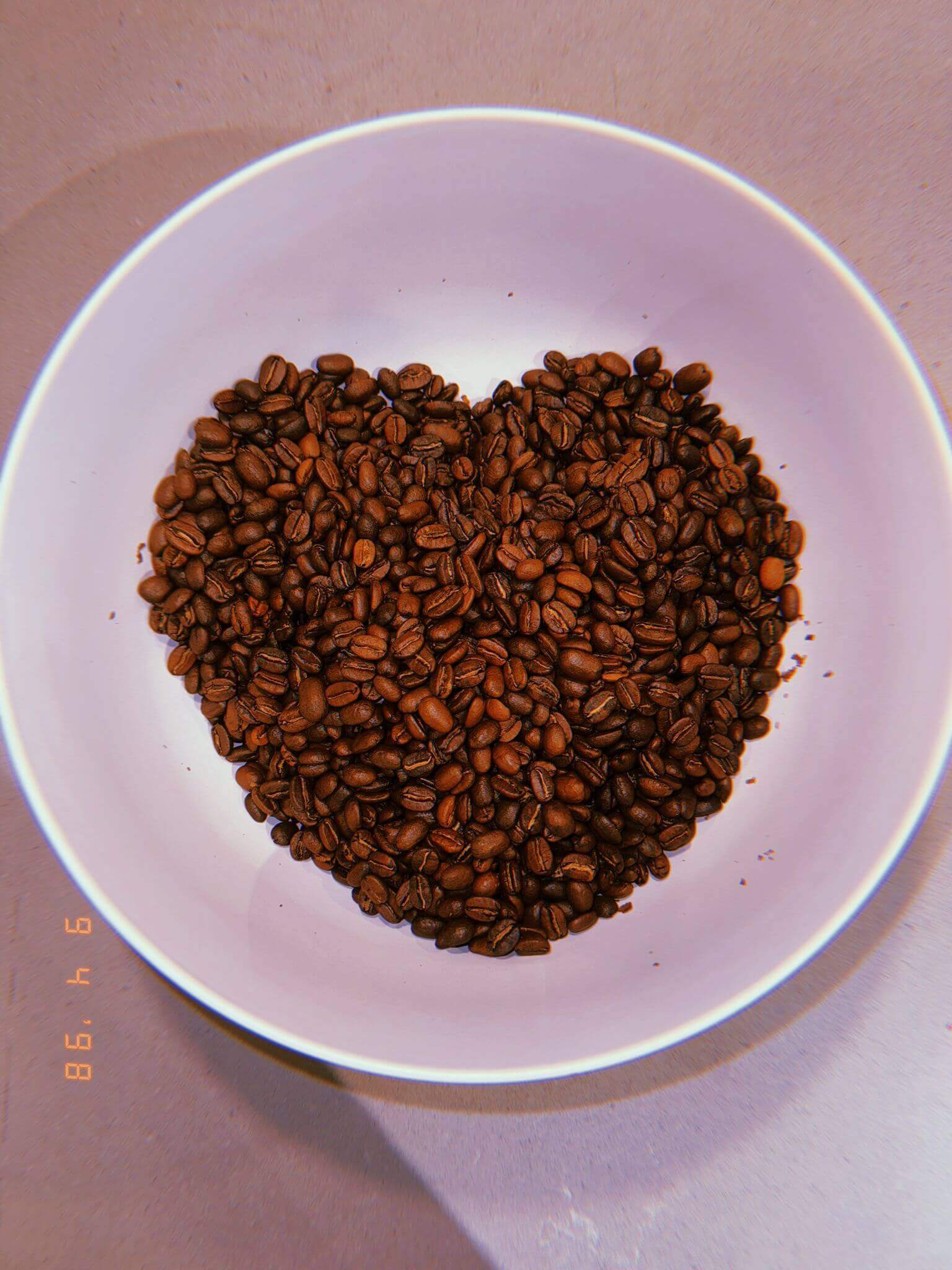 Heart-shaped arrangement of premium Arabica coffee beans in a white bowl for Naturally Flavored Almond Delight Coffee.