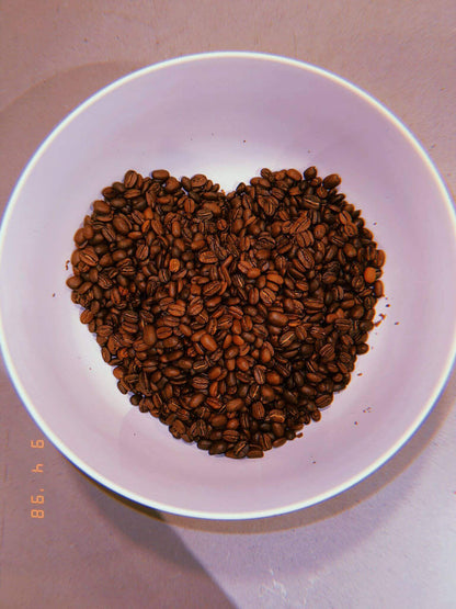 Heart-shaped coffee bean arrangement in white bowl, highlighting the rich texture of naturally flavored almond coffee beans.